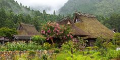 an old village with thatched roofs and flowers in the foreground, surrounded by mountains