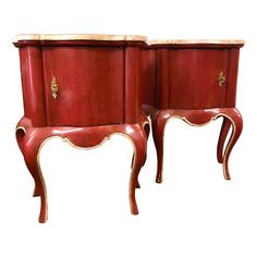 two red wooden tables with gold trimmings on each side and one has an open drawer