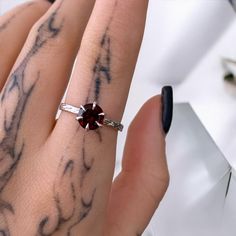 a woman's hand with tattoos and a ring on her left wrist, holding a red diamond