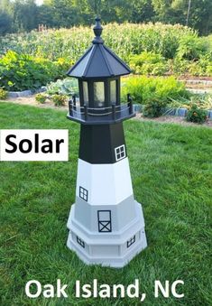 a black and white light house sitting in the grass next to a field with plants