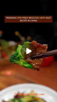 the broccoli and beef is being held up by chopsticks over a white plate