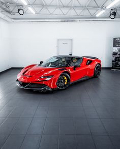 a red sports car is parked in a large room with white walls and black flooring