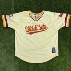 a baseball jersey that is laying on the ground with grass in front of it and wild cats written across the chest