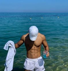 a shirtless man standing in the ocean holding a water bottle