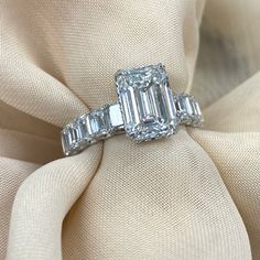 an emerald cut diamond ring on top of a white cloth