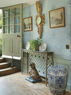 a room with blue and white wallpaper, an ornate console table and pictures on the wall