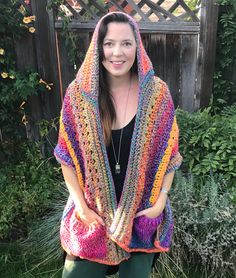 a woman wearing a colorful crochet shawl in front of a wooden fence