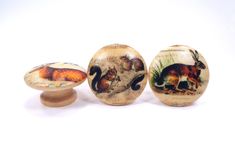 three wooden knobs with animals painted on them are lined up against a white background