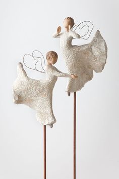 two white figurines on top of wooden sticks with hearts in the shape of angels