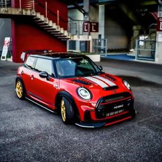 a red and white mini with gold rims parked in front of a building next to stairs