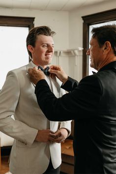 a man helping another man put on his bow tie