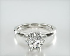 a white gold engagement ring with a round brilliant cut diamond in the center, on a plain surface