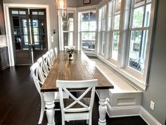 a dining room table with white chairs next to a large window and wooden flooring