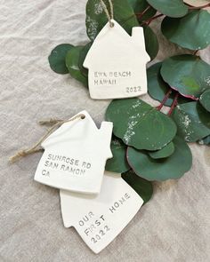 three ceramic tags with names on them sitting next to some leaves and plants in the sand