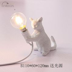 a small white cat lamp with a light bulb on it's back paws up