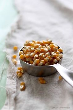 a metal spoon filled with corn kernels on top of a white cloth covered table