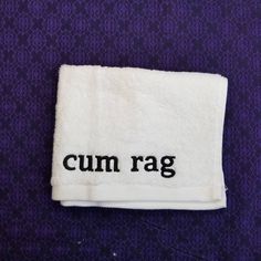 a white towel with the word cumrag on it sitting on top of a purple carpet