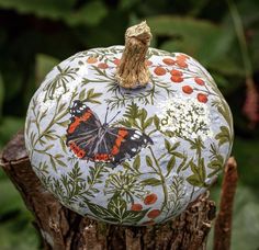 a painted pumpkin sitting on top of a tree stump in front of some leaves and flowers