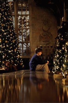 a man sitting on the floor next to a christmas tree in a room filled with lights