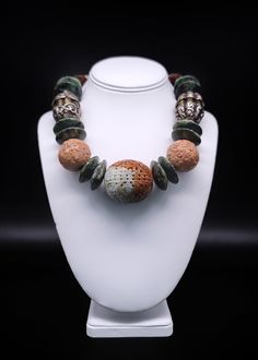 "Description and Details  A symphony of 27 unique beads, each one interesting on its own, blended into a statement of complementary color, form, and texture. The middle stone is an oversized carved two-colored jade longevity beads surrounded by large aventurine spacers, carved wooden longevity beads, Tibetan Silver, and gilt beads, smaller carved Jade longevity beads, natural turquoise beads, more jade, and finally a sterling silver box clasp with an inlaid tiger eye stone. This piece is a conve Nature-inspired Necklace With Large Beads For Gifts, One Of A Kind Green Round Bead Jewelry, Unique Green Carved Necklace, Round Carved Agate Necklaces, Unique Carved Round Beads Jewelry, Large Jade Bead Jewelry, Carved Agate Round Necklaces, Unique Jewelry With Carved Round Beads, Unique Jewelry With Large Beads