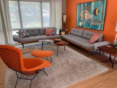 an orange and gray living room with two couches, chairs, coffee table and painting on the wall