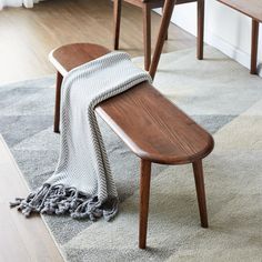 a wooden bench sitting on top of a rug next to a chair and table with a blanket