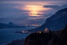 the sun is setting over some mountains with water and lights in the foreground, as seen from an overlook point