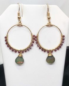 Ethiopian Opal and Garnet when paired with 14k Gold Filled components result in a elegant pair of earrings! ❤️ MATERIALS USED      ▪️Ethiopian Opals: These smooth, opaque stone flash shades of red, orange            and green. The stones measure 8mm (w) x 8mm (h).      ▪️Garnet: These dark red, round, faceted stones measure 2mm.      ▪️14k Gold Filled: The wire and ear wire are Gold Filled. ❤️ MEASUREMENTS       ▪️The hand shaped hoop measures 7/8" in diameter. With the garnet stones,            the hoop measures 1-1/16" diameter. ❤️ LENGTH      ▪️ The earring hangs 1-7/16" from the bottom of the ear wire and 2-1/4" from the             top of the ear wire. ❤️ PROCESSING TIME      ▪️The item will be processed and shipped within 1-3 business days from the                   time the order is Christmas Celebration Jewelry With Matching Earrings, Elegant Christmas Jewelry With Dangle Shape, Elegant Christmas Drop Earrings, Elegant Christmas Jewelry With Matching Earrings, Handmade Round Jewelry For Christmas, Elegant Round Christmas Earrings, Handmade Round Christmas Jewelry, Small Hoop Gemstone Earrings For Gift, Adjustable Wire Wrapped Earrings For Anniversary