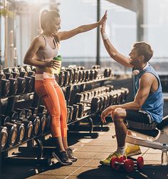 a man and woman sitting on benches in a gym with dumbbells behind them