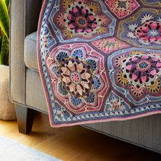 a crocheted blanket is sitting on a couch next to a potted plant