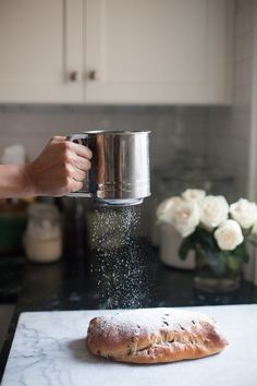 a person pouring sugar over a pastry on top of a counter next to white flowers