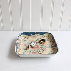 two wedding rings are placed in a decorative tray on a white tablecloth with striped wallpaper