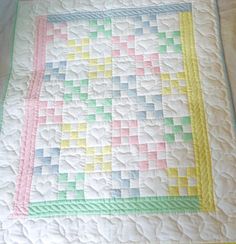 a quilted blanket on top of a bed with white sheets and pink, green, blue, yellow, and orange squares