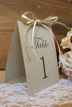 a table number is tied with twine and sits on a lace doily next to flowers