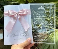 a hand holding up a wedding card with a pink bow on it and the front