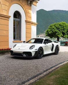 a white sports car is parked in front of a building with mountains in the background