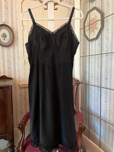 This is a beautiful, medium weight, satiny feeling polyester black slip or slip dress, trimmed with black lace on the bust and bottom edge. The measurements, taken with the slip lying flat, are: armpit to armpit/bust, 19 inches; waist, 17 inches; length, 41 inches (from top of strap); bottom edge, 28 inches. In very good condition. Lace Slip Dress With Built-in Bra For Daywear, Black Dress With Built-in Bra For Night, Black Lace Trim Dress For Night, Black Lace Camisole With Spaghetti Straps, Elegant Black Slip Dress With Contrast Lace, Black Dress With Bias Cut And Spaghetti Straps, Black Satin Camisole Dress, Black Camisole Slip Dress, Black Bias-cut Dress With Spaghetti Straps