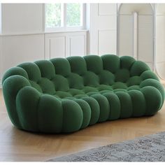 a green couch sitting on top of a hard wood floor next to a rug and window