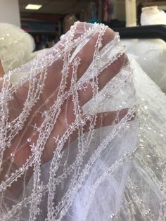 a woman's hand is covered with white beads and mesh fabric, while she sits in a chair