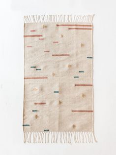 a beige rug with multicolored stripes and fringes on it, against a white background