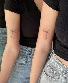 two women with tattoos on their arms and one has a small bow at the top