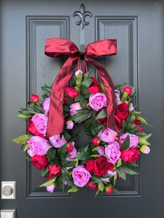 a wreath with pink and red flowers is hanging on the front door