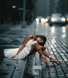 a woman is sitting on the ground in the rain with her arms around her head