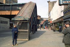 a man standing on the side of a road next to a tall building with a metal roof