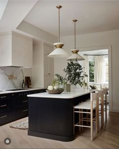 a kitchen with black and white cabinets, an island table and two pendant lights hanging from the ceiling