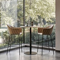 two chairs sitting at a table in front of a glass wall with trees outside the window