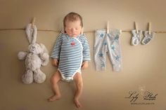 a baby sleeping next to two teddy bears on a clothes line with pegs hanging from it