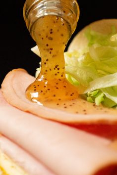 a sandwich with lettuce, ham and mustard being drizzled onto it