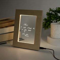 an illuminated photo frame on a desk with a plant in the background and a quote written inside