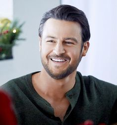 a man with a goatee smiles at the camera while sitting in front of a christmas tree